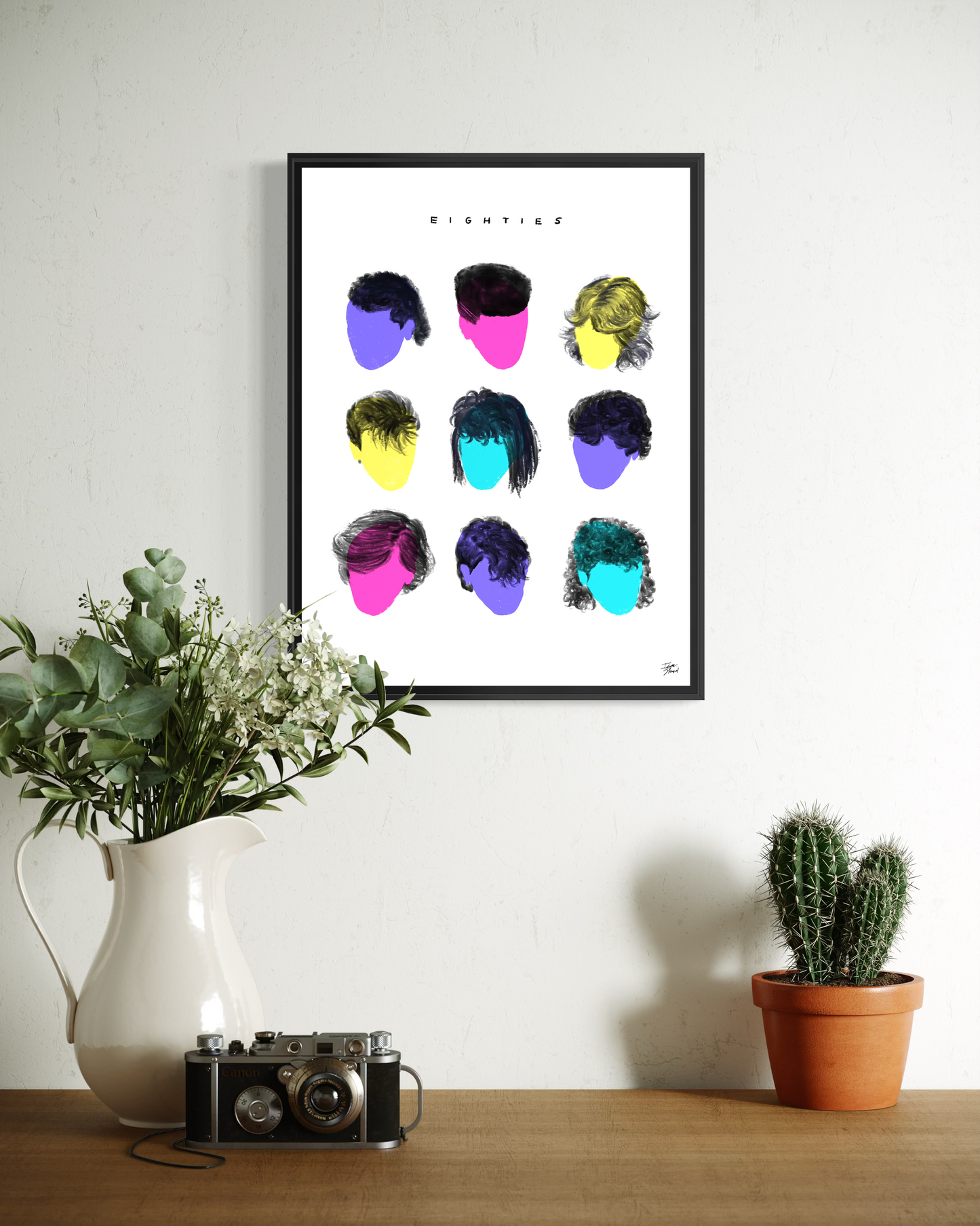 Minimalist 80s hairstyles art print in a sleek aluminum frame. The colorful typographic grid hangs above a clean white floating shelf holding a stack of books and a black vintage-style camera. An industrial-chic studio setup.
