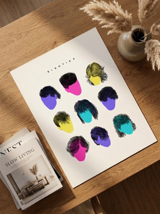 A high-fidelity, natural-light top-down view of the EIGHTIES // 1984 Archival Edition unframed art print, featuring colorful 3x3 grid of geometric hairstyle silhouettes. The premium matte paper print is displayed flat on a rich natural oak wood table, styled with dried pampas grass in an artisanal ceramic vase and a stack of 'Slow Living' magazines. A curated museum-quality artifact by Vaykay-Idanshani.